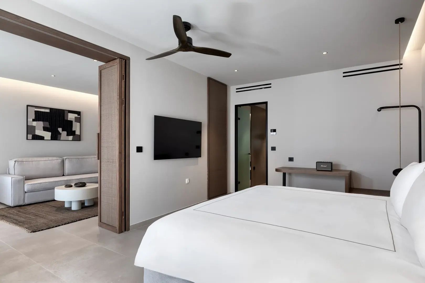 Modernes Schlafzimmer einer Suite mit Flachbild TV, Deckenventilator und Schiebetür zum Wohnbereich.