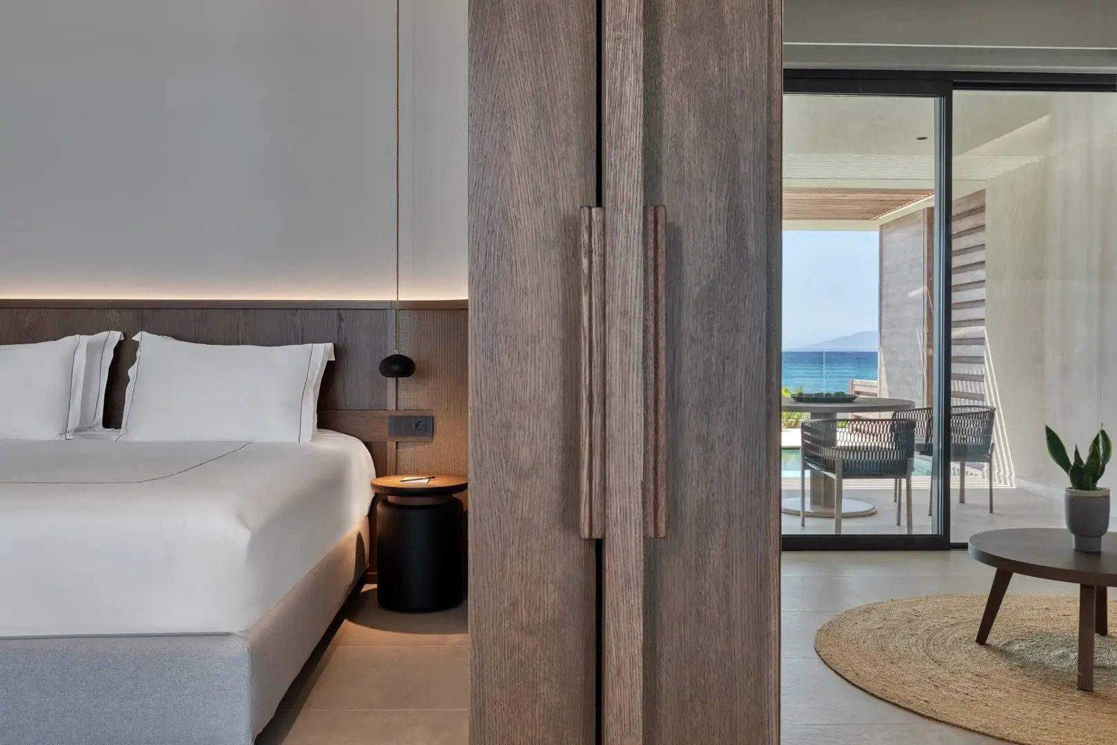 Modern eingerichteter Schlafbereich einer Suite mit Holzschrank und Blick ins Freie.