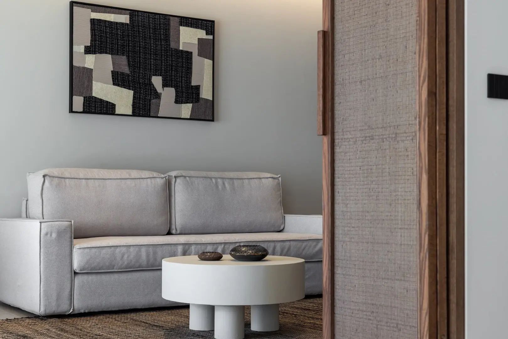 Sitzecke im Wohnbereich mit hellem Sofa, rundem Couchtisch und einem abstrakten Wandbild.