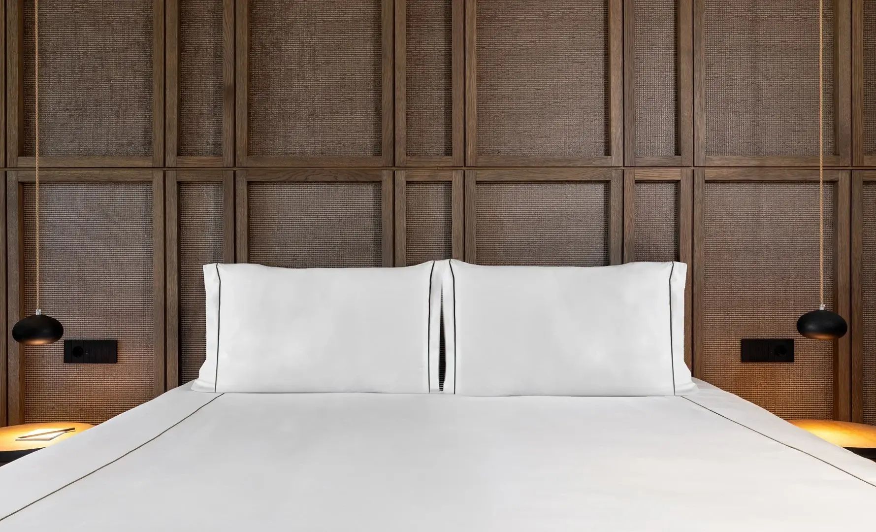 Nahaufnahme von zwei weißen Kissen auf einem Bett vor einer braunen Holzstruktur.