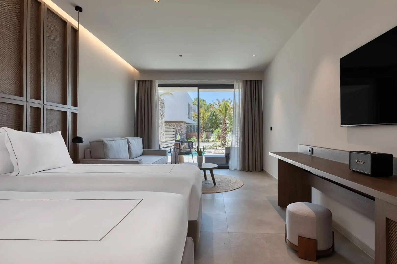 Hell eingerichtete Suite mit Doppelbett, Sofa, Schreibtisch und Blick auf die Terrasse.