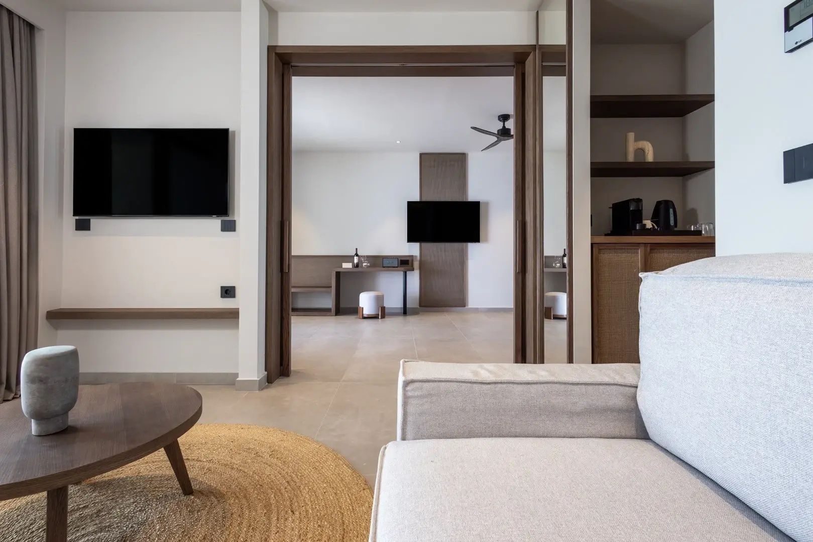 Wohnzimmer einer Suite mit hellem Sofa, Holzschiebetür und Blick in ein weiteres Zimmer.