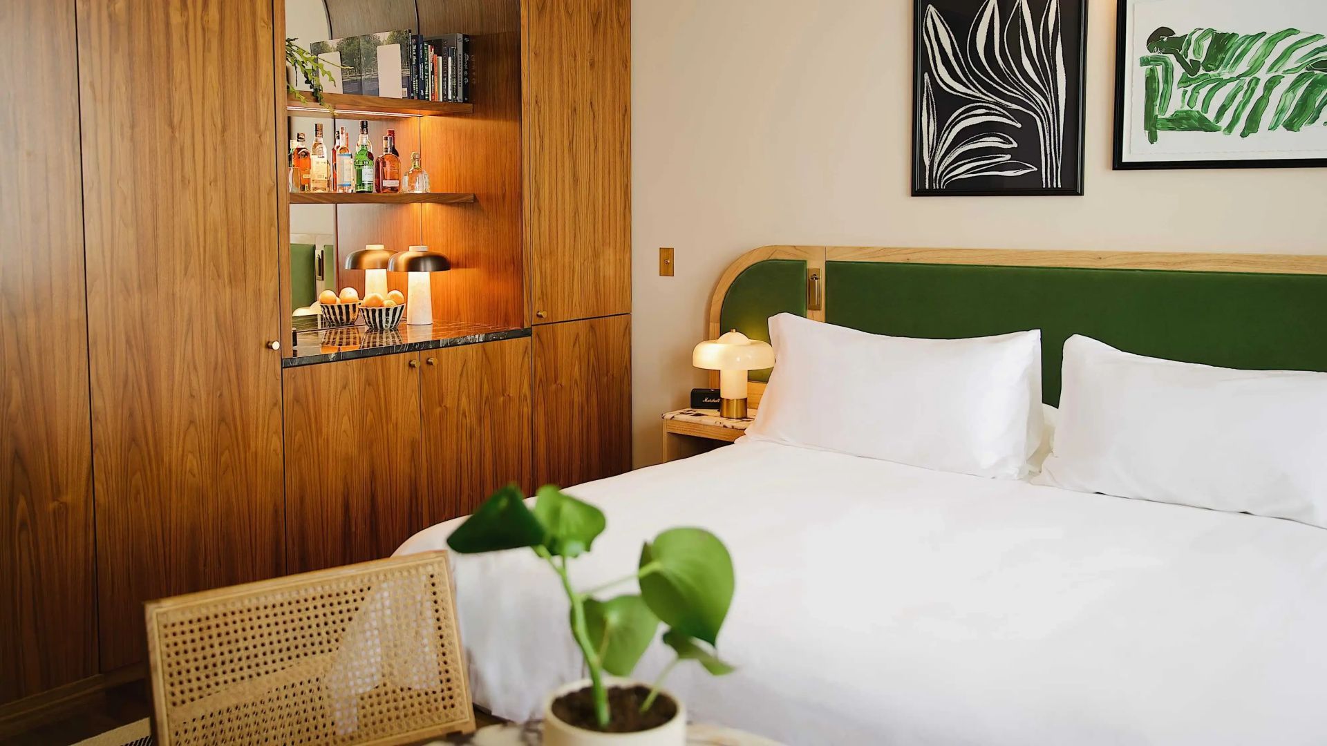 Hotelzimmer mit weißem Bett, Nachttischlampe und Holzschrank mit Minibar.
