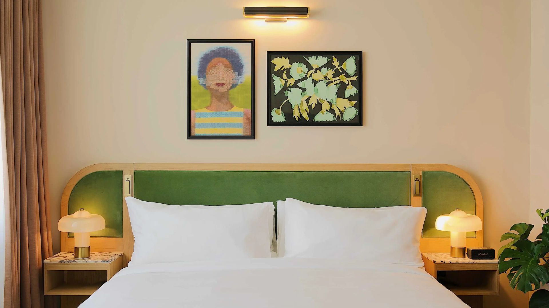 Weiße Kissen auf einem Bett unter zwei eingerahmten Kunstwerken an der hellen Wand.