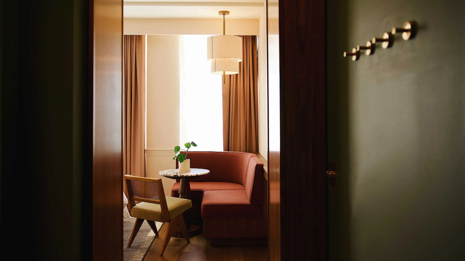 Sitzbereich im Zimmer mit rotbrauner Eckbank, rundem Tisch und Vorhängen.