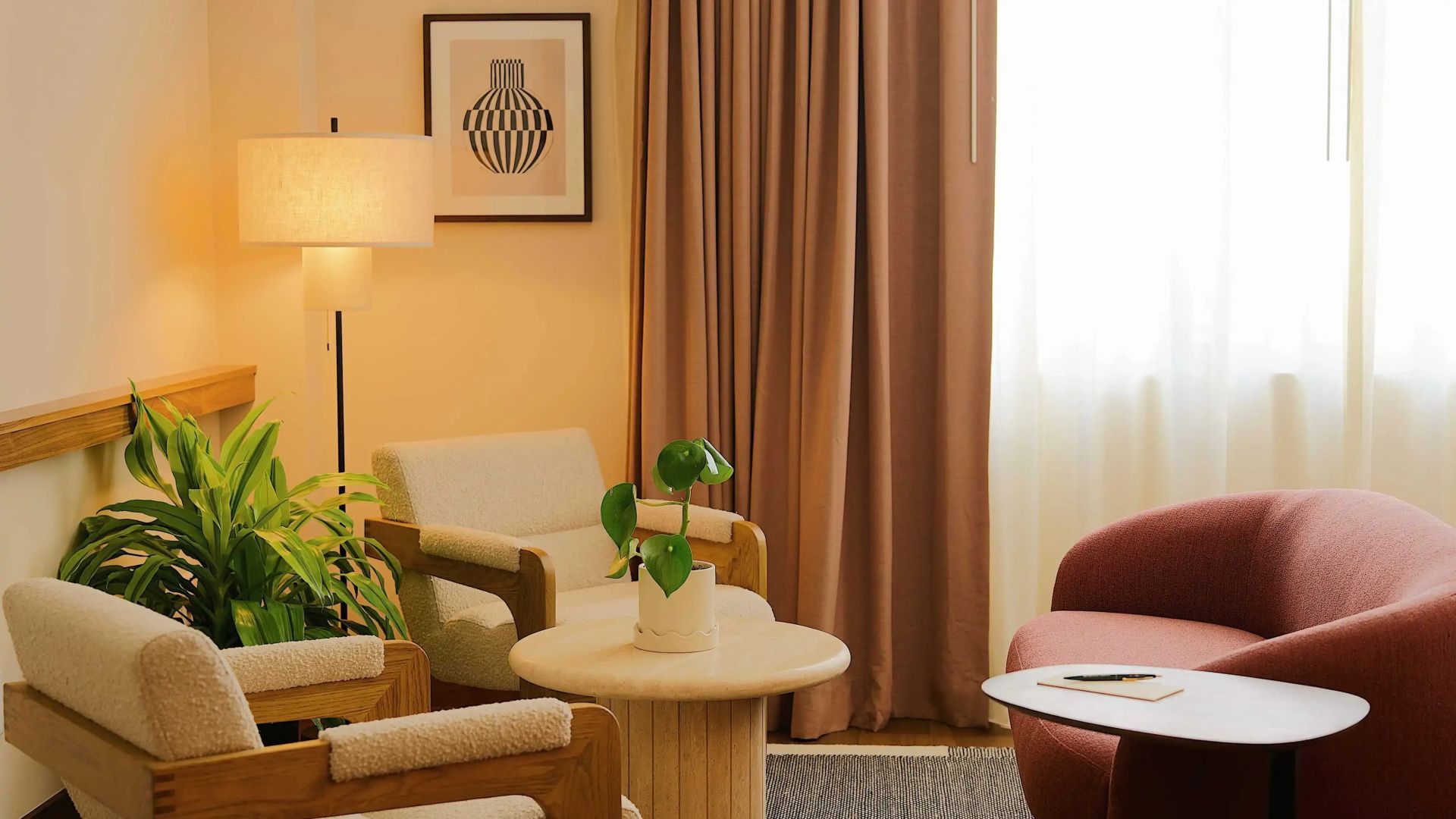 Sitzbereich im Zimmer mit beigen Sesseln, rundem Holztisch und braunen Vorhängen.