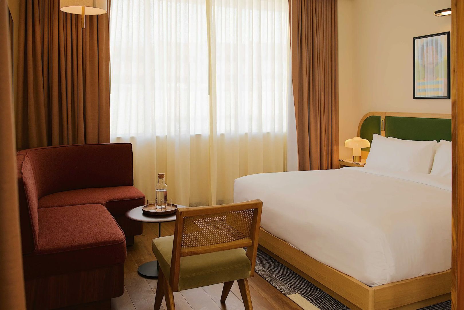 Sitzbereich im Hotelzimmer mit braunem Sofa, Holzstuhl und Fenster mit Vorhängen.