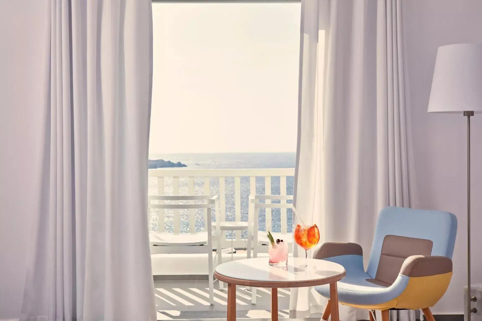 Blick durch die Balkontür mit Getränken auf dem Tisch auf das nahe Meer.