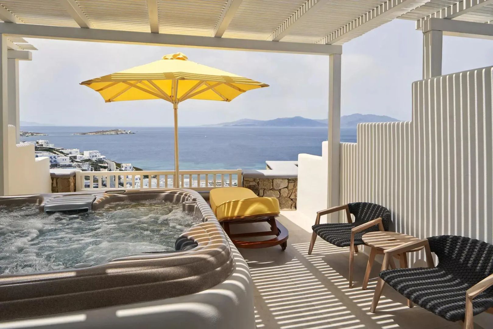 Überdachte Terrasse mit Whirlpool, gelbem Sonnenschirm, Liege und Blick auf das Meer.