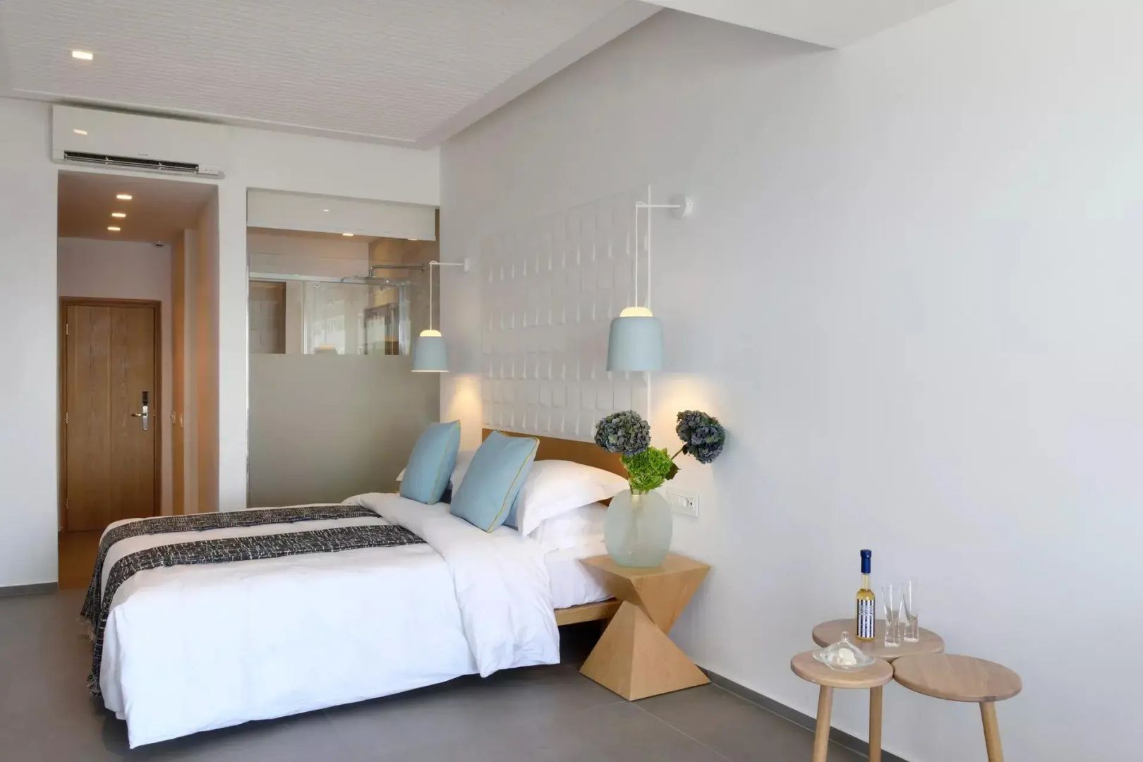 Hell eingerichtetes Hotelzimmer mit Doppelbett, blauen Kissen und stilvollen Hängelampen.