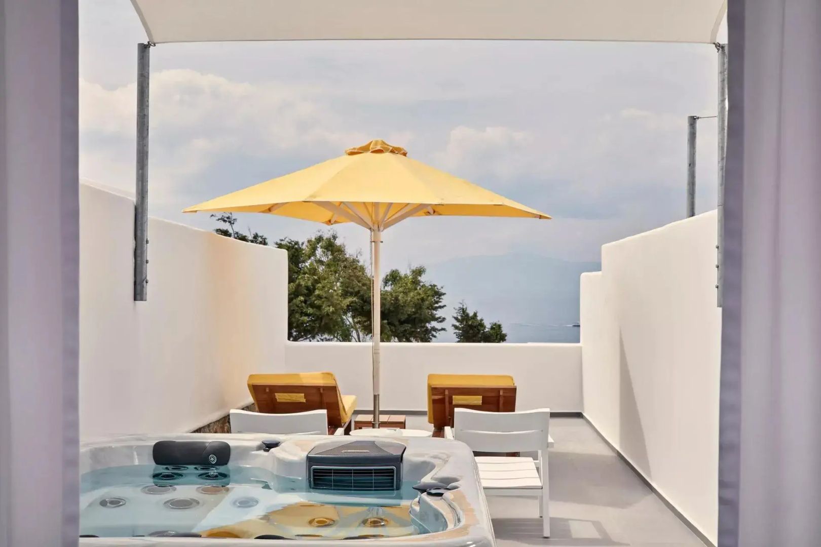 Sonnige Terrasse mit Whirlpool, gelbem Sonnenschirm, Liegen und Blick auf das Ägäische Meer.