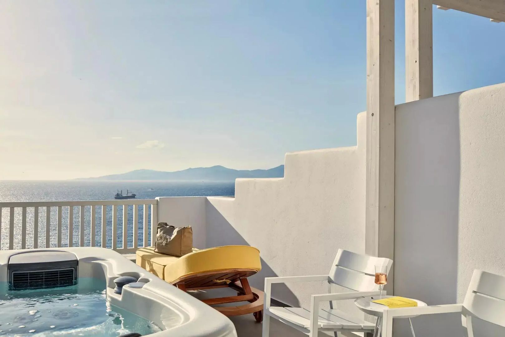 Terrasse mit Jacuzzi, gelber Sonnenliege und freier Sicht auf das blaue Meer und die Küste.