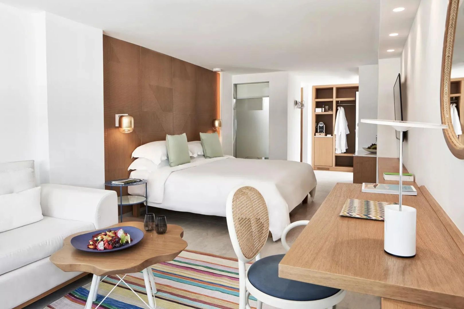Helles Hotelzimmer mit großem Doppelbett, Schreibtisch und Sitzbereich mit Couch.