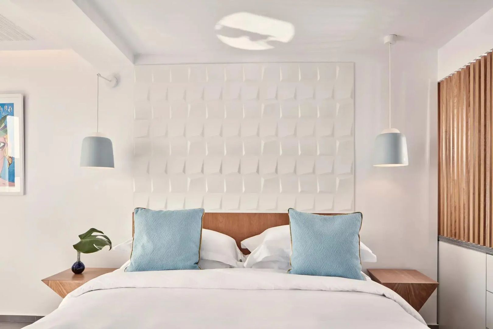Doppelbett mit weißer Bettwäsche, zwei hellblauen Kissen und einer strukturierten Wand.