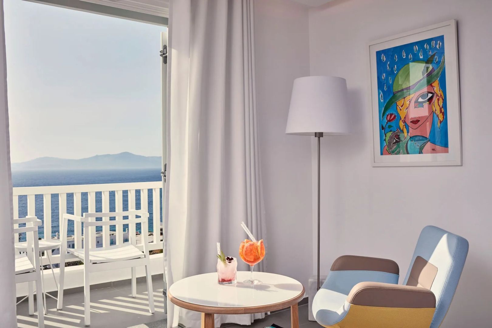 Blick durch die offene Balkontür eines Hotelzimmers auf das Meer mit einem kleinen Tisch im Vordergrund.