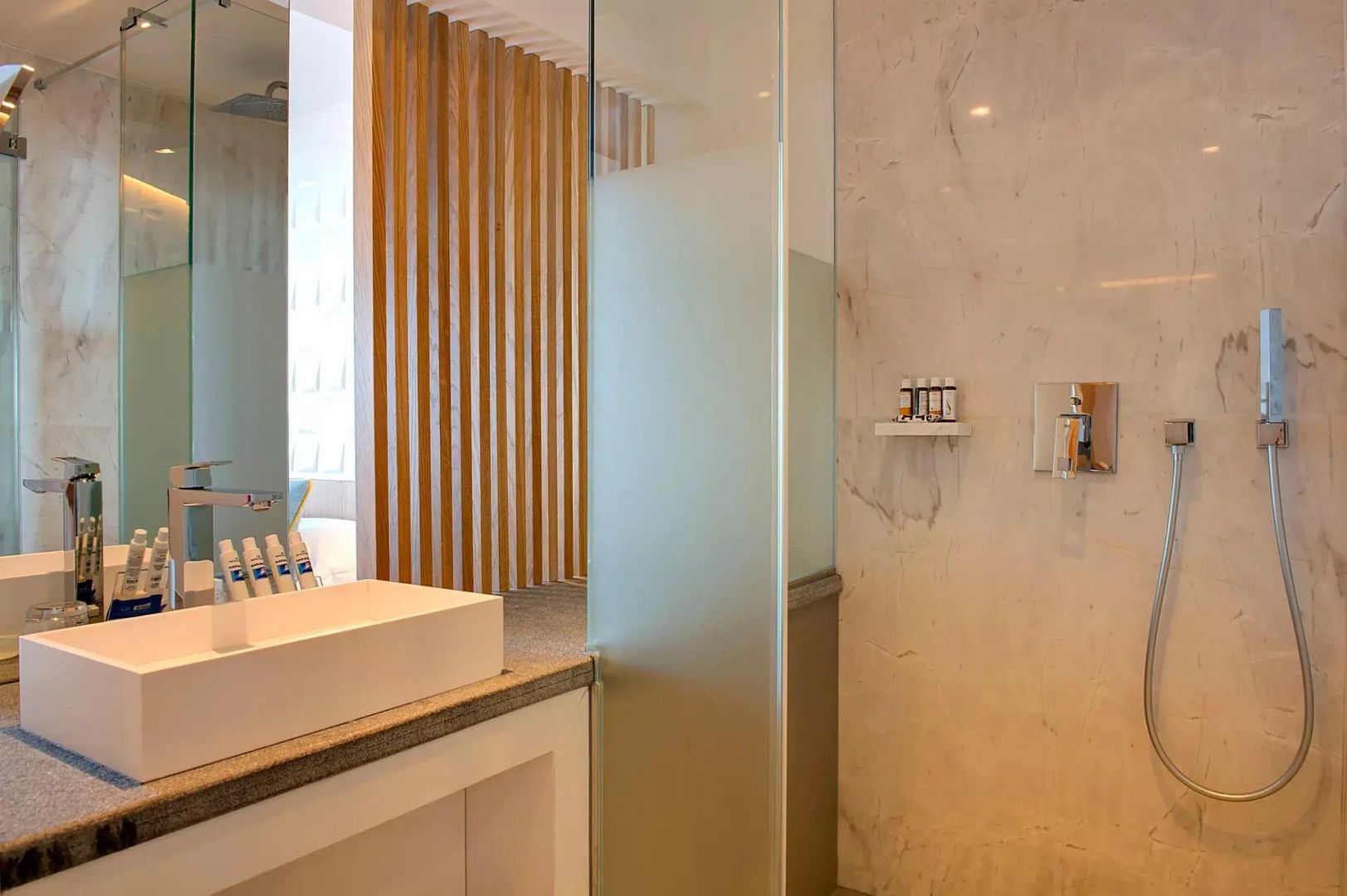 Badezimmer mit weißem Waschbecken, Glastrennwand und Marmorwand in der Dusche.