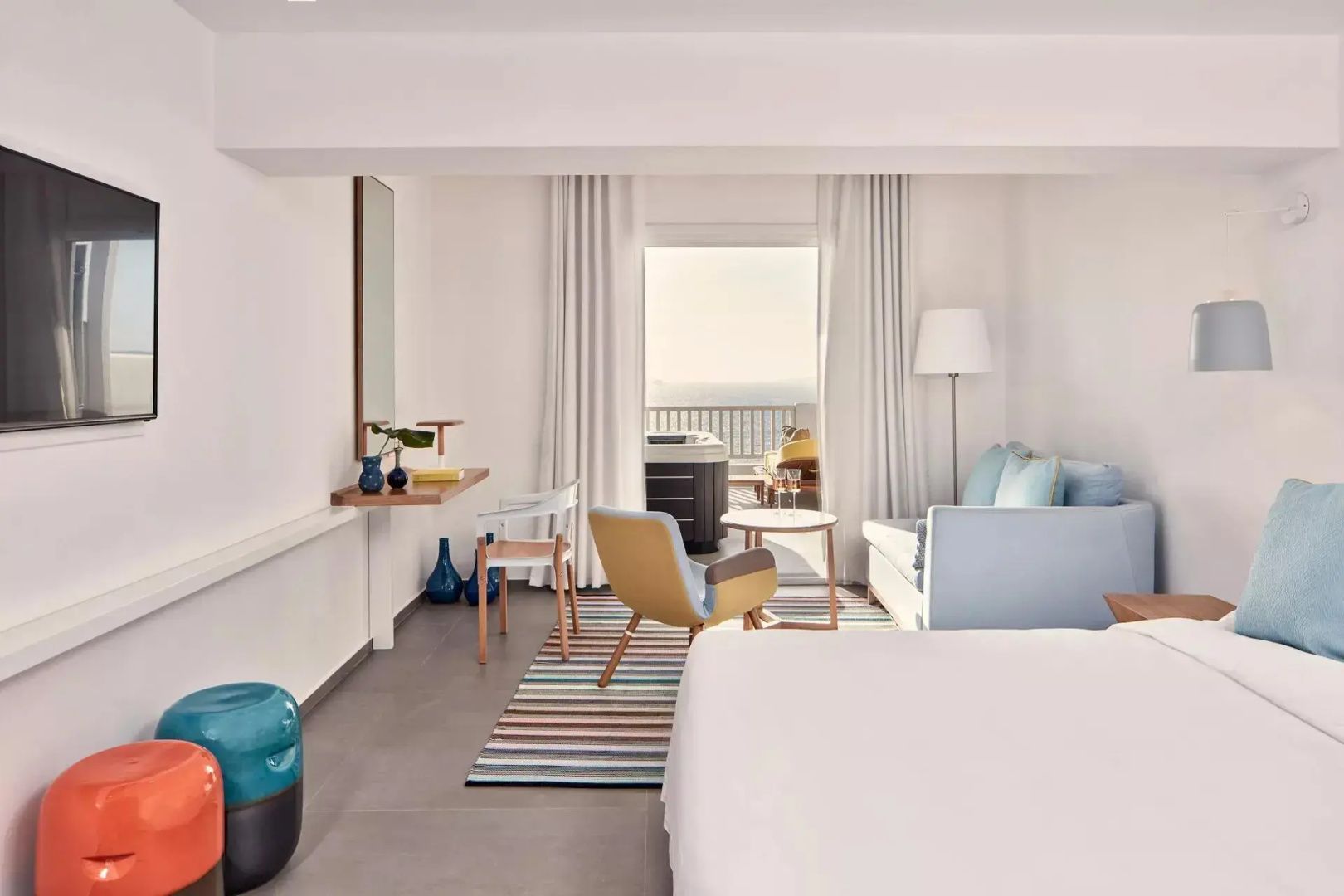 Geräumiges Hotelzimmer mit hellem Sofa, Sessel, buntem Teppich und Blick auf das Meer.
