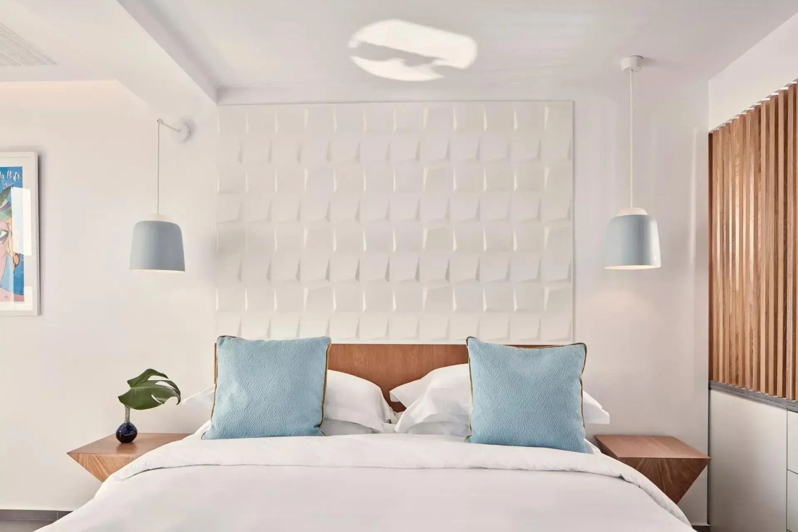 Doppelbett mit hellblauen Kissen, Pendelleuchten und strukturierter Wand.