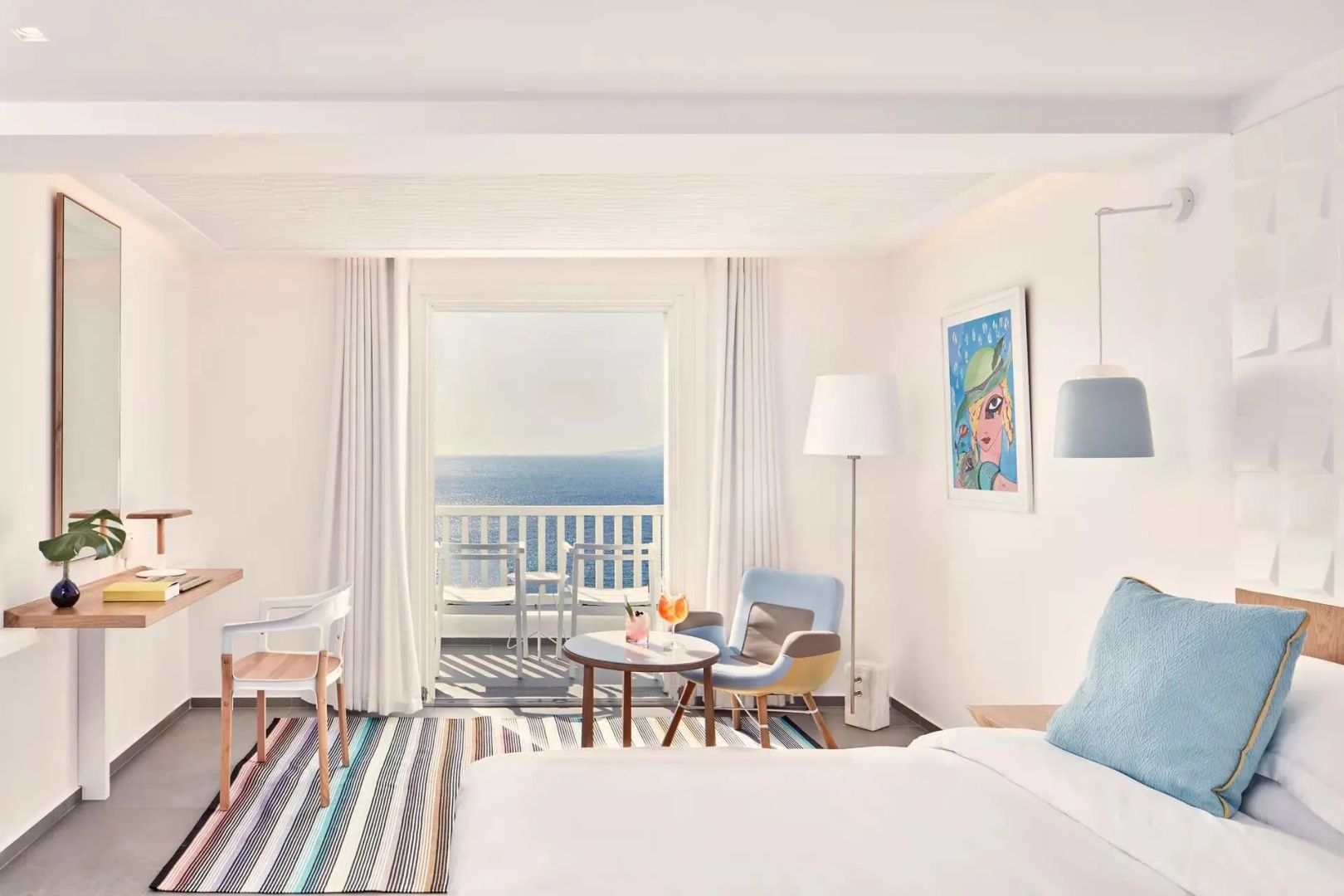 Hotelzimmer mit Sitzbereich, buntem Teppich und Balkon mit Blick auf das Meer.