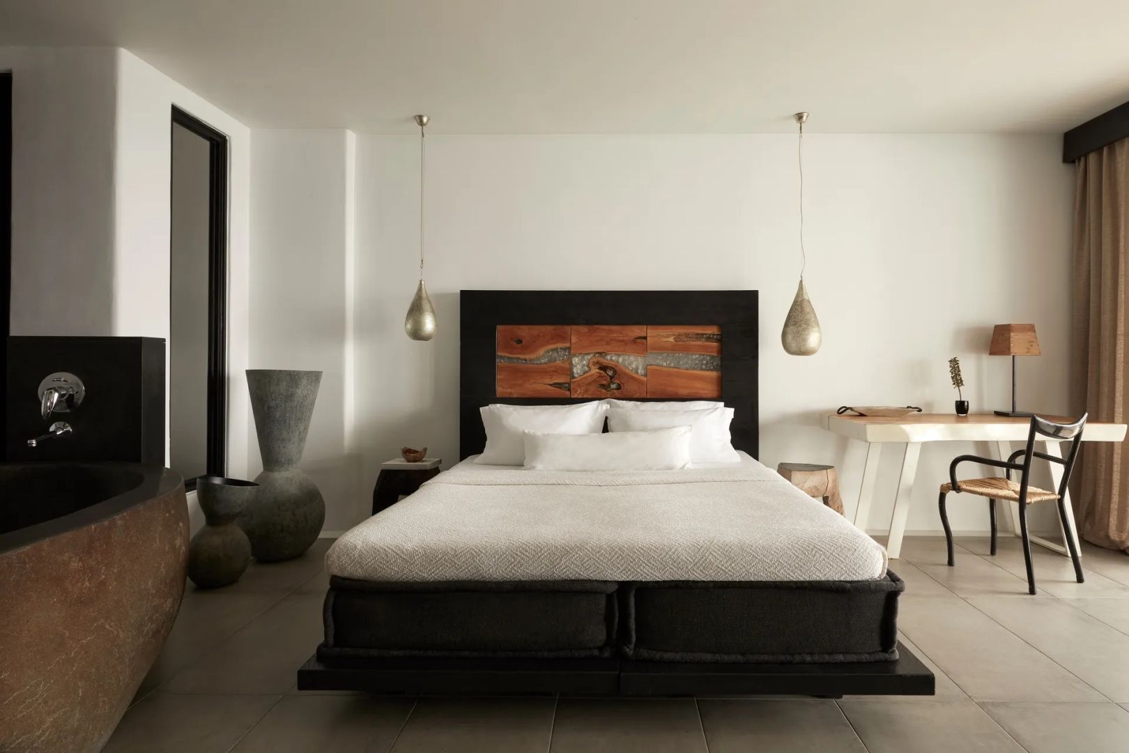 Doppelbett mit weißer Bettwäsche, dunklem Kopfteil und hängenden Leuchten im Hotelzimmer.