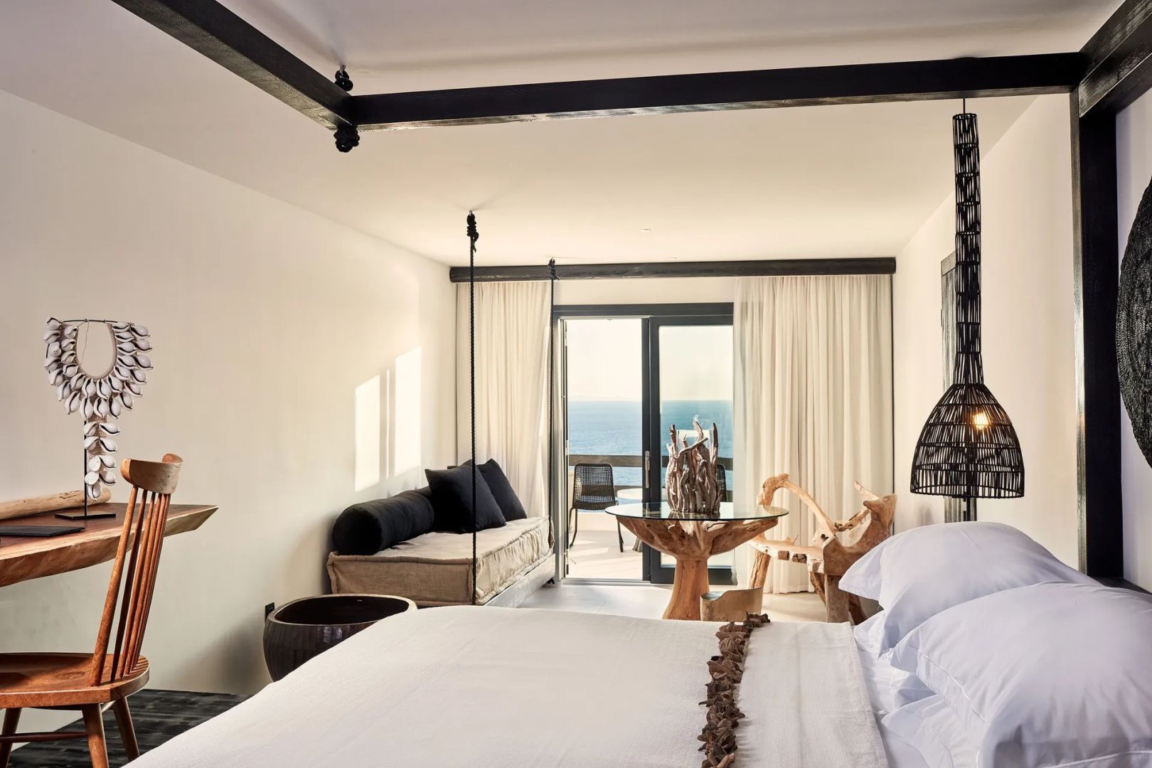 Helles Hotelzimmer mit Doppelbett, Hängesofa und Blick aufs Meer.