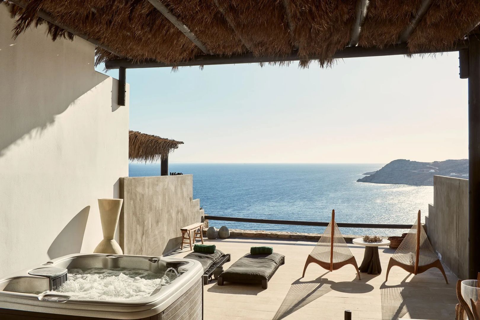 Whirlpool auf einer sonnigen Terrasse mit Holzmöbeln und Weitblick aufs Meer.
