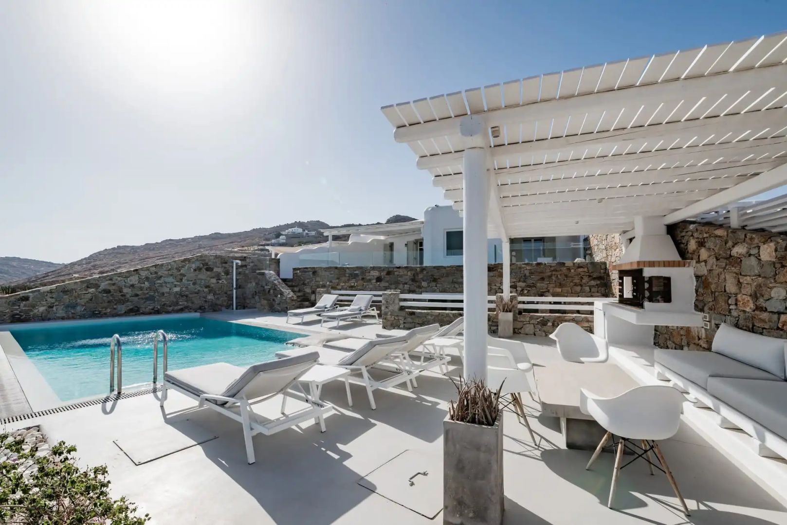 Sonnendeck am Pool mit mehreren Sonnenliegen, Pergola und Blick auf die umliegenden Hügel.