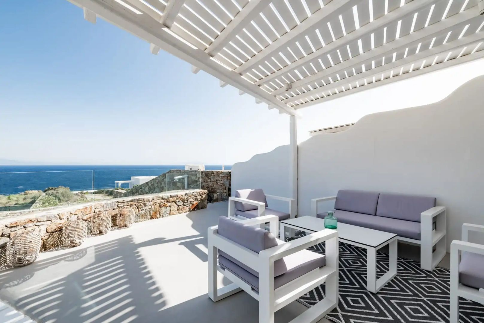 Überdachte Terrasse mit grauen Sitzmöbeln, Holztisch und weitem Blick auf das Ägäische Meer.