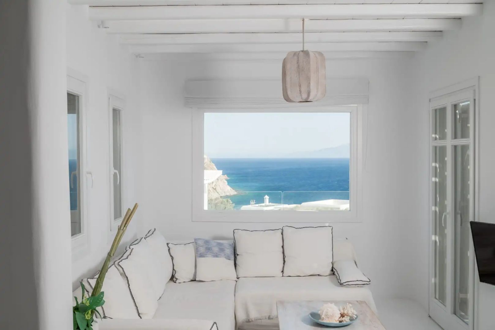 Sitzbereich mit weißem Sofa vor einem großen Fenster mit direktem Blick auf das Meer.