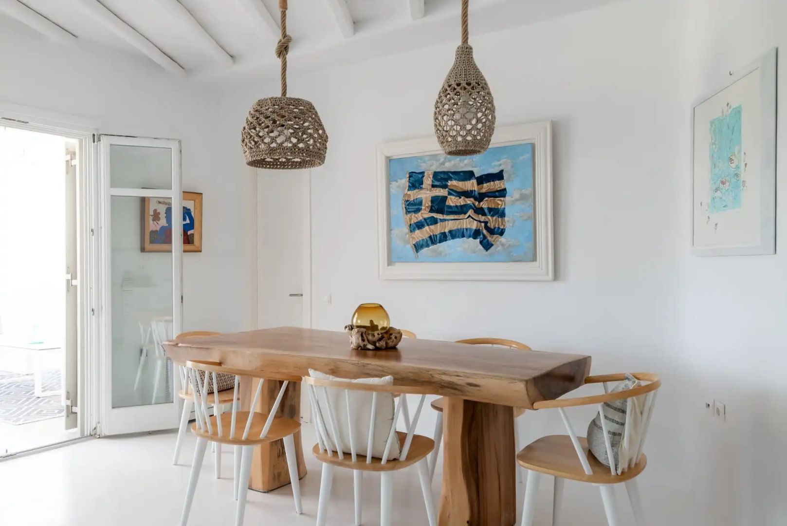 Essbereich mit Holztisch, Stühlen und Flechtlampen vor einer weißen Wand mit Bild.