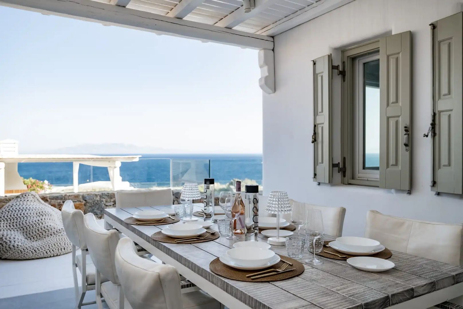 Gedeckter Esstisch auf einer überdachten Terrasse mit freiem Blick auf das blaue Meer.