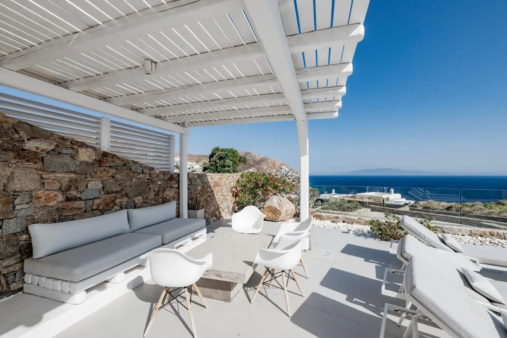 Sitzbereich im Freien mit weißer Pergola, Steintisch und Blick auf die Küste.