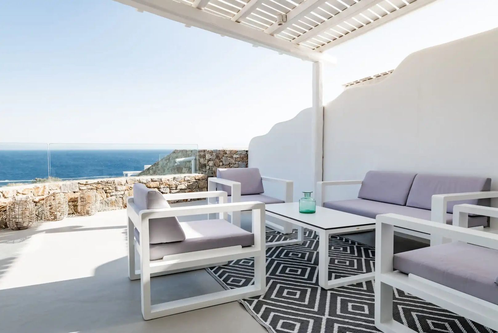 Überdachte Terrasse mit hellen Sitzmöbeln, Teppich und freiem Blick auf das blaue Meer.
