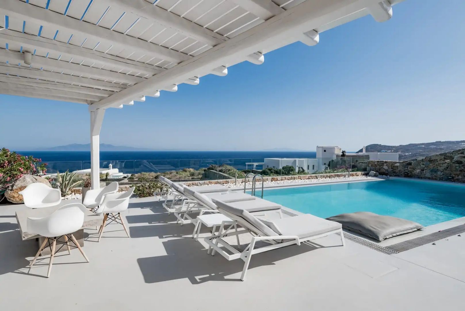 Sonnenliegen und Sitzgruppe unter einer Pergola am Pool mit Blick auf das Meer.