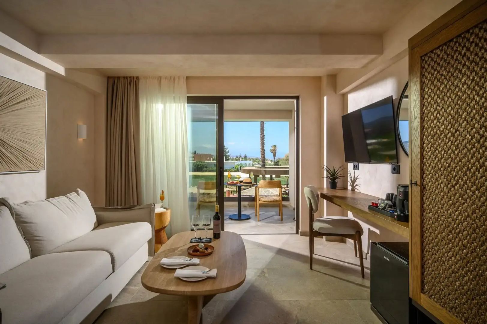 Wohnbereich eines Zimmers mit Sofa, Couchtisch, Fernseher und Terrassenausgang.