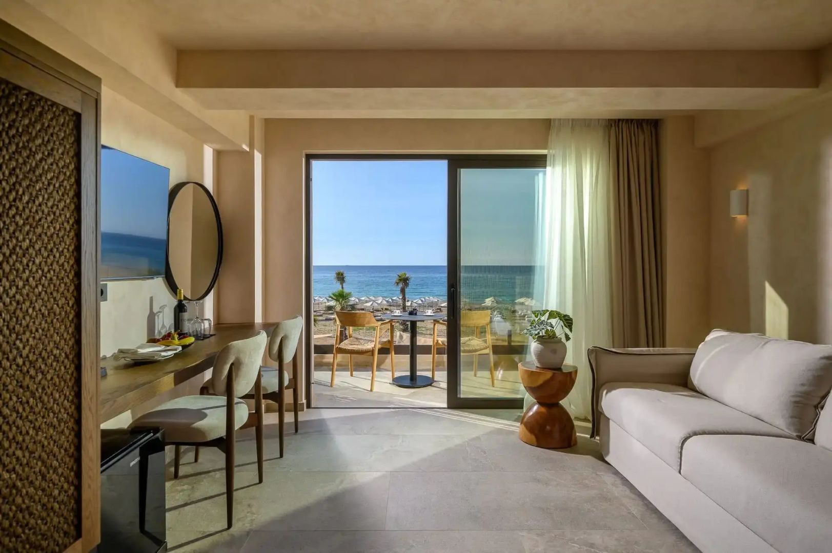 Hotelzimmer mit Schreibtisch, Sitzbereich und Blick durch die Balkontür auf das Meer.