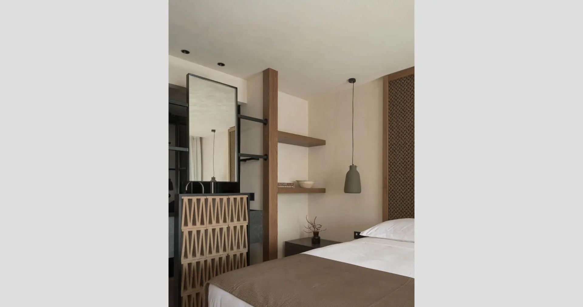 Bett und angrenzender Waschtischbereich mit Holzrahmen und hängender Lampe im Hotelzimmer.