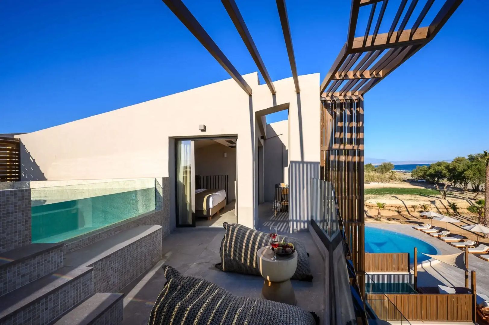 Sonnige Dachterrasse mit Sitzkissen, Holzpergola und Blick auf den Pool sowie das Meer.
