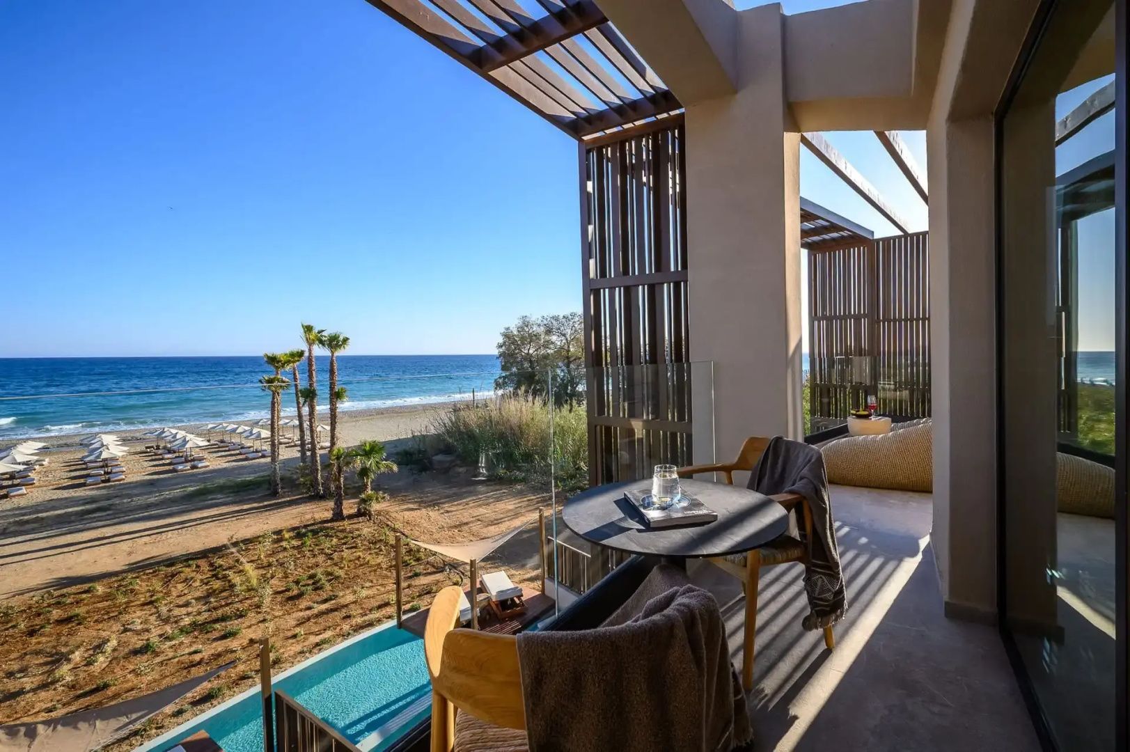 Balkon mit Tisch und Stühlen sowie direktem Blick auf den Strand, Palmen und das Meer.