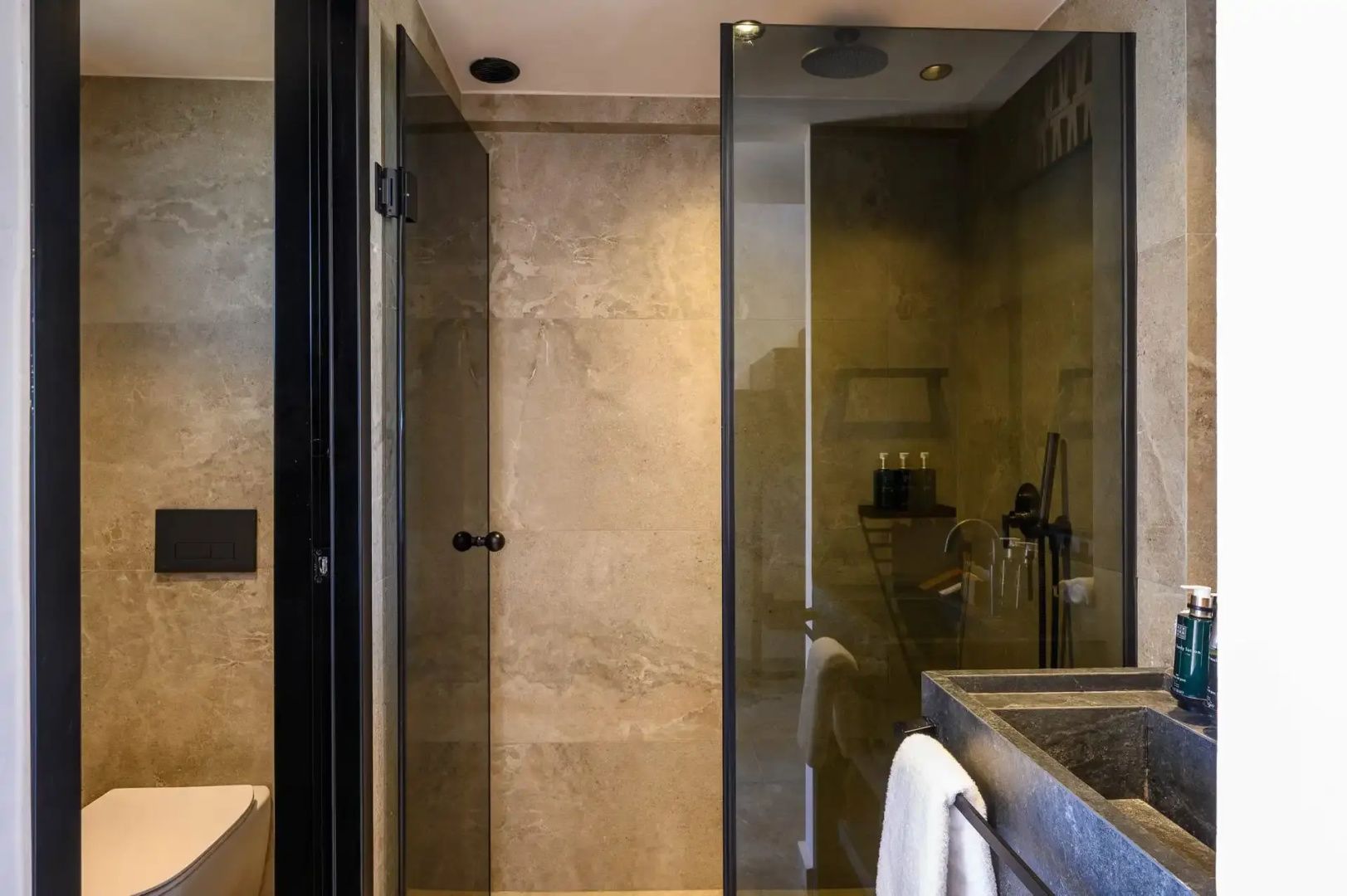 Badezimmer mit moderner Glasdusche, dunklen Natursteinwänden und Waschtisch.