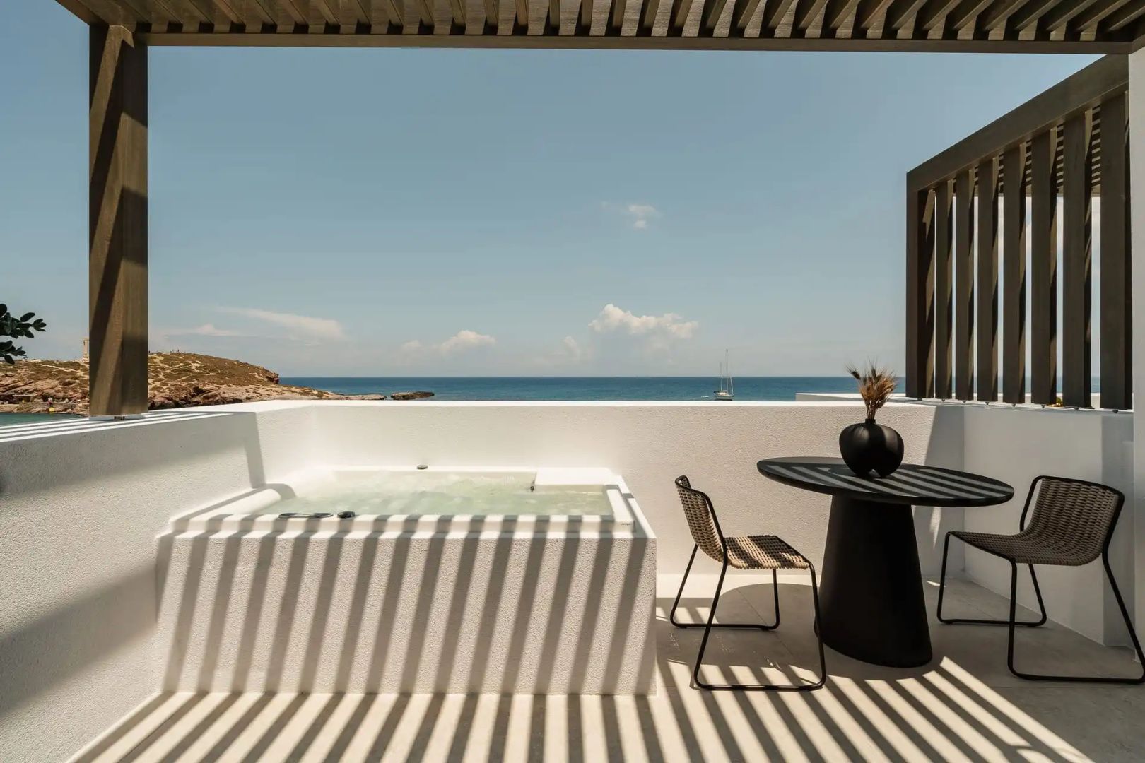 Überdachte Terrasse mit Whirlpool, Tisch, Stühlen und Blick auf das blaue Meer.
