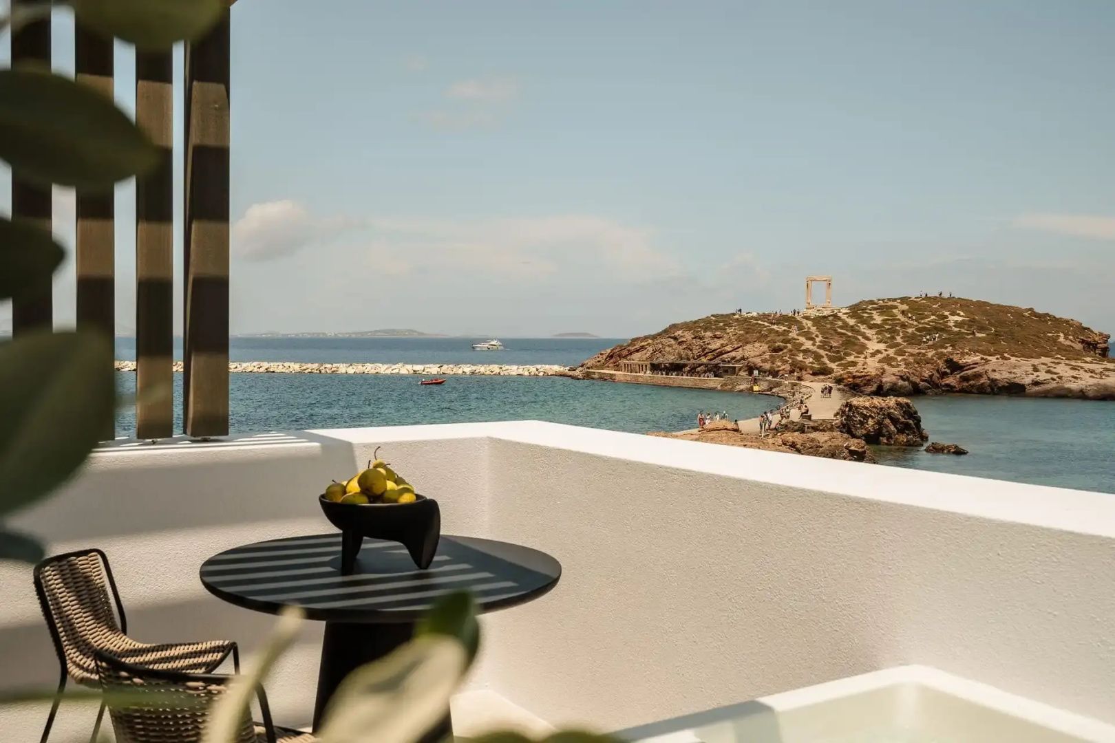 Terrasse mit Tisch und Obstschale sowie Blick auf das Meer und die Tempelruine Portara.