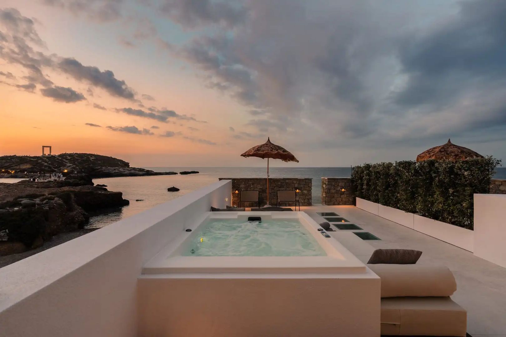 Terrasse mit integriertem Whirlpool, Sonnenschirm und freiem Blick auf das Meer bei Dämmerung.