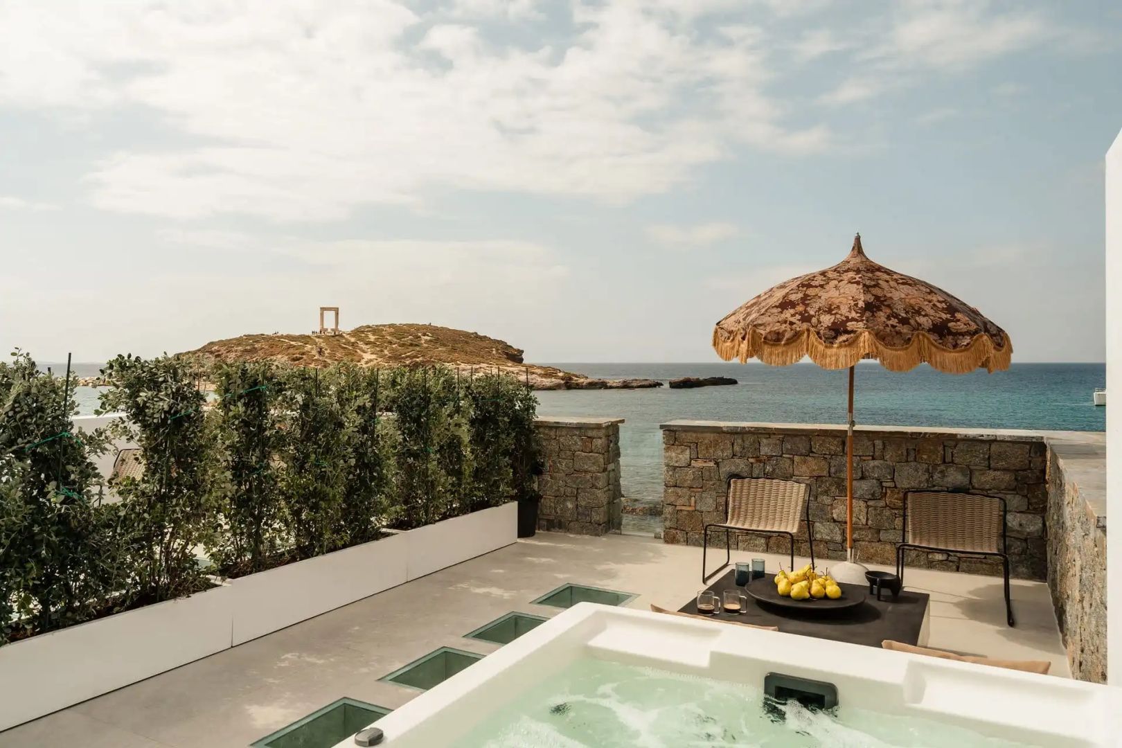 Terrasse mit Whirlpool, Sonnenschirm und Blick auf das Meer sowie die Portara von Naxos.