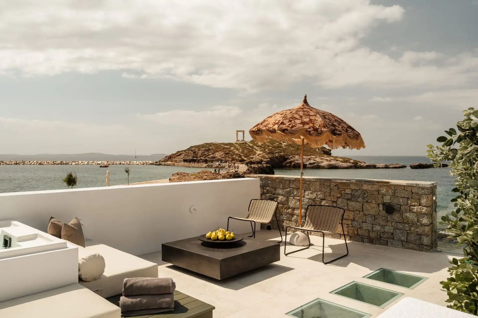 Terrasse mit Sonnenschirm und Blick auf das Meer sowie die historische Tempelruine im Hintergrund.