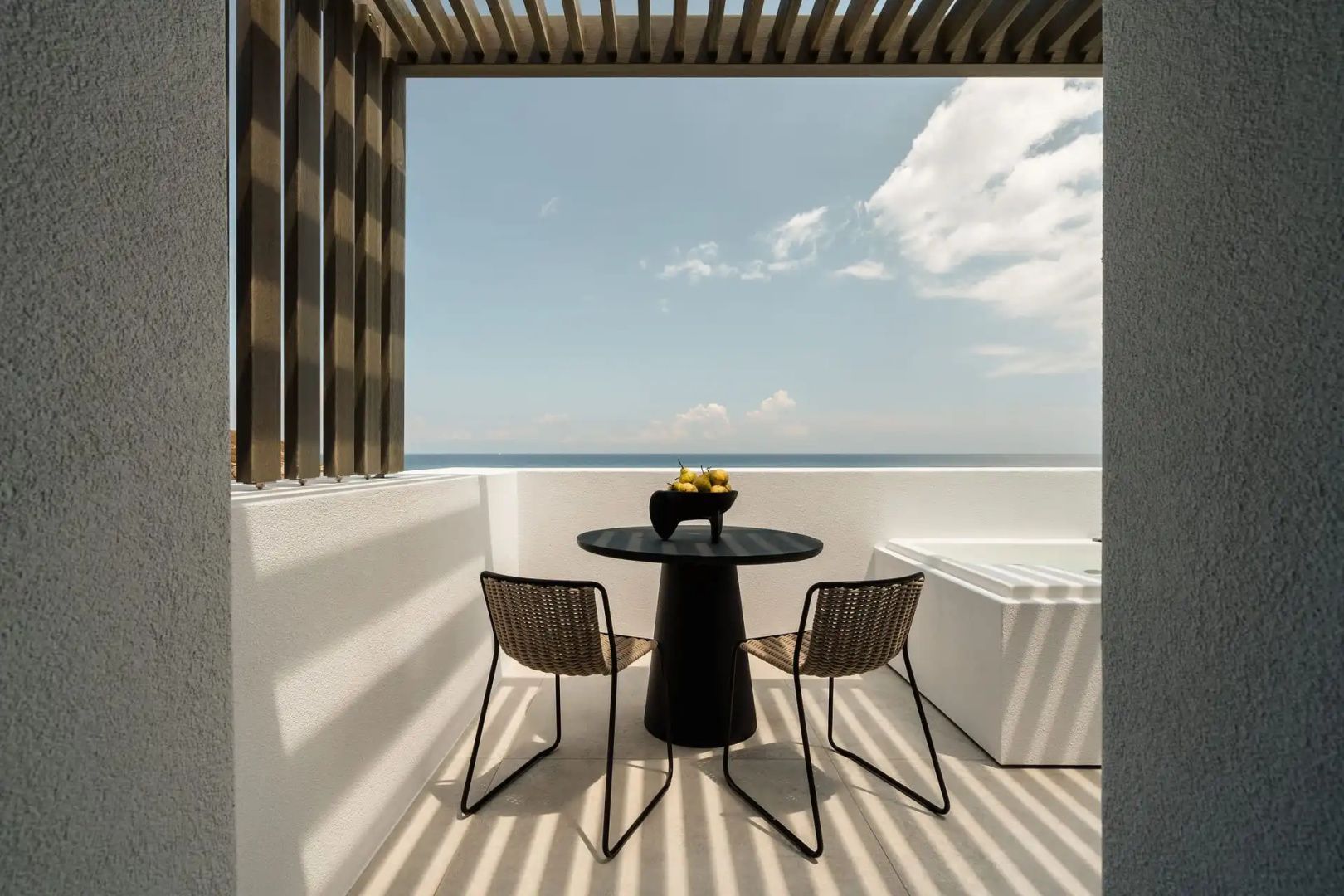 Terrasse mit Pergola, schwarzem Tisch, Stühlen, Whirlpool und freiem Meerblick.