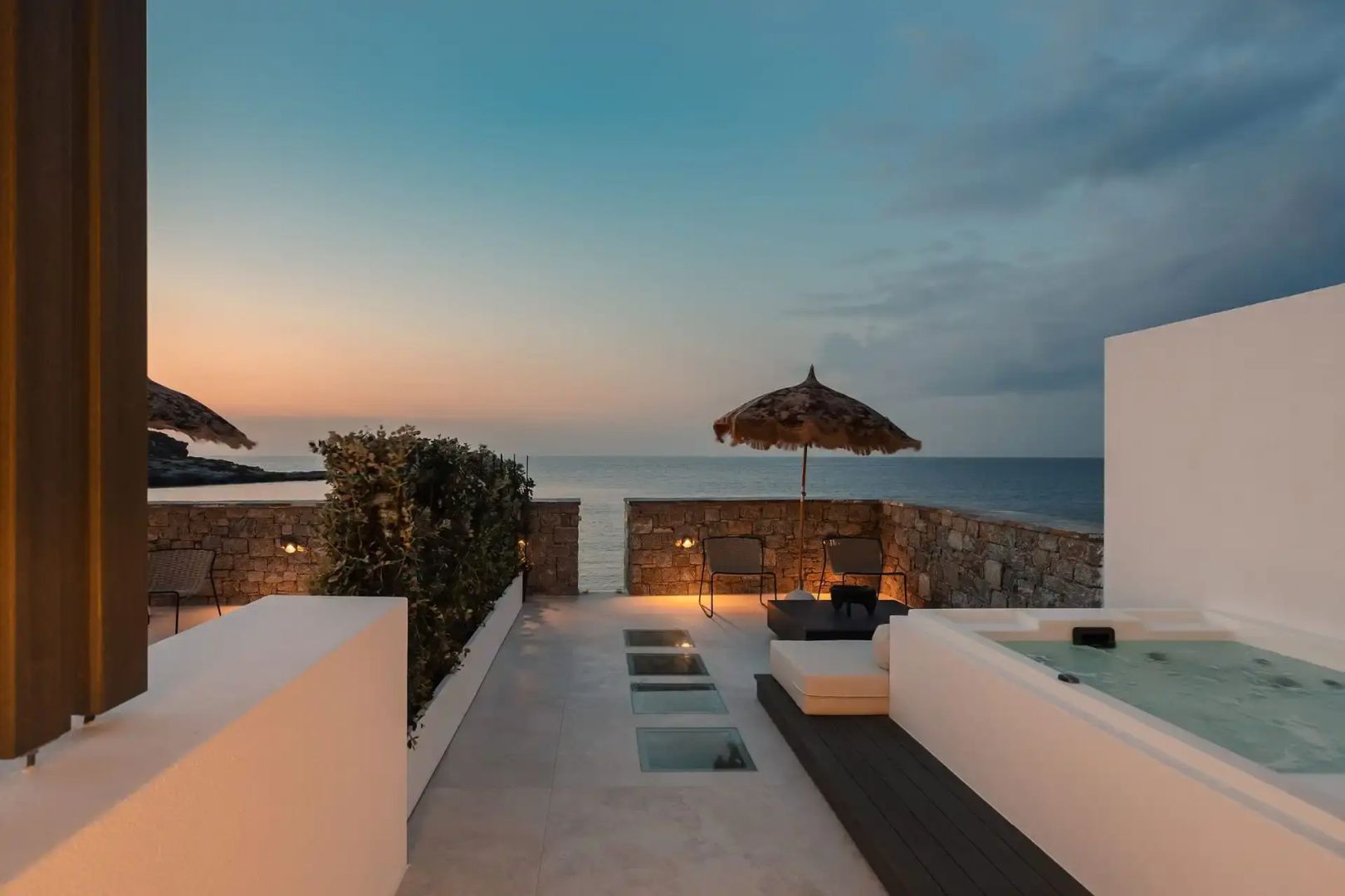 Dachterrasse bei Dämmerung mit Whirlpool, Sonnenschirm und direktem Blick auf das Meer.
