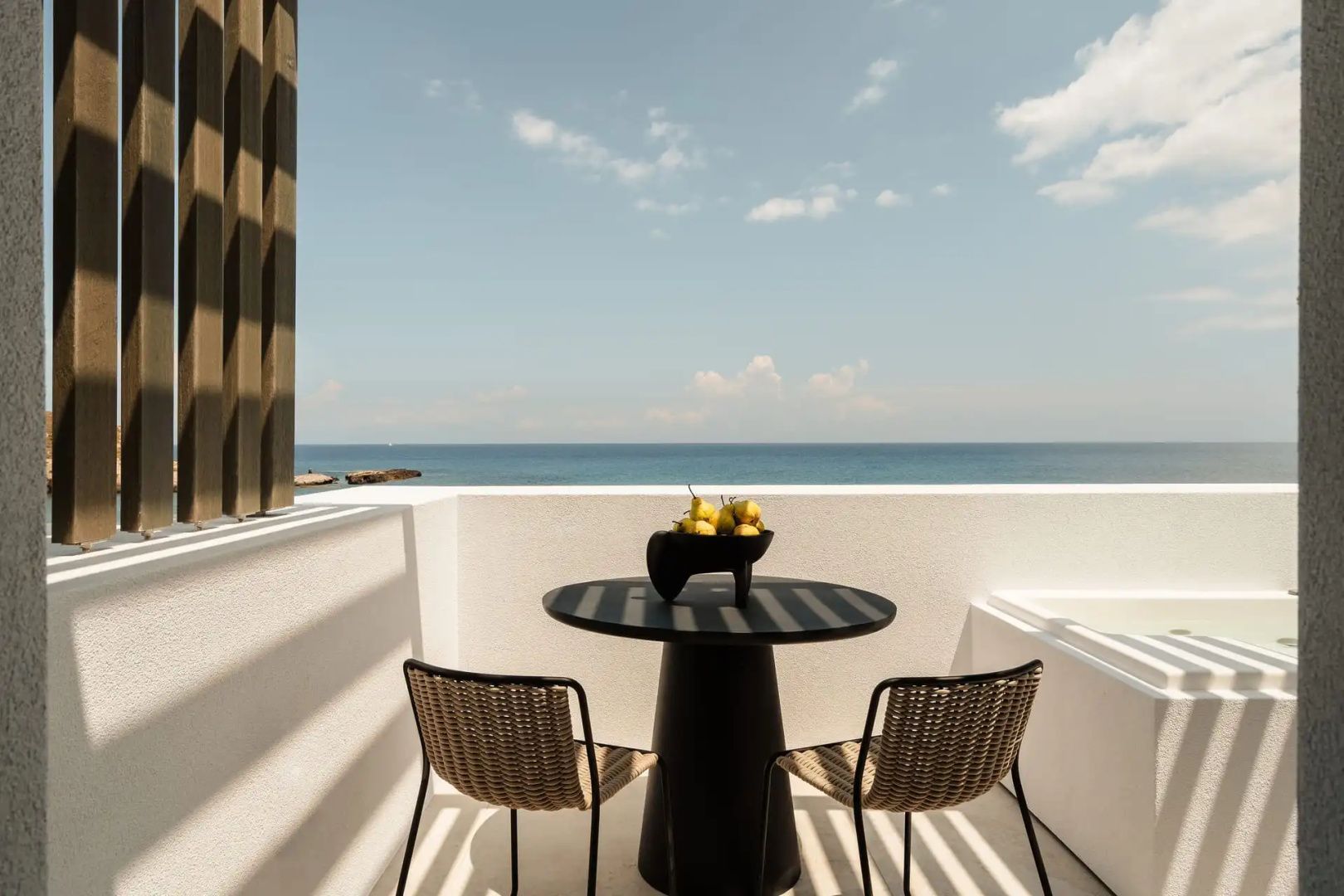 Balkon mit einem runden Tisch, zwei Stühlen, Obstschale und Blick auf das Meer.