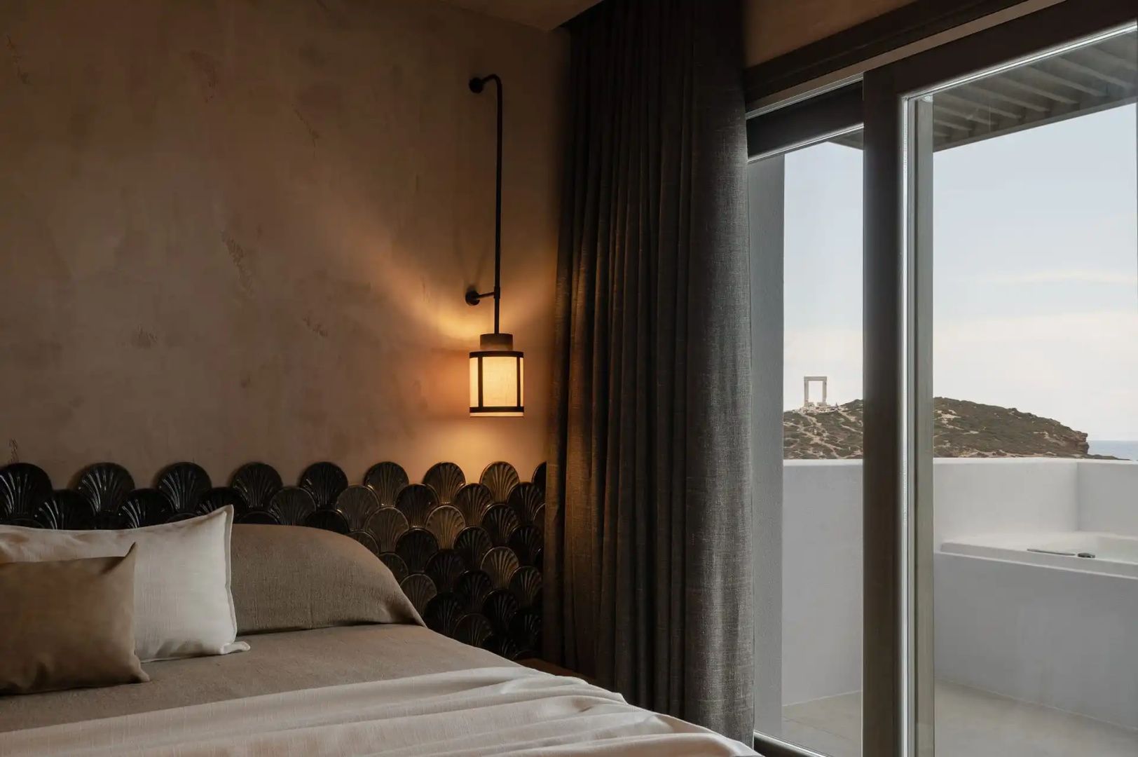 Schlafbereich mit Bett, Hängeleuchte und Fenster mit Blick auf die Landschaft von Naxos.