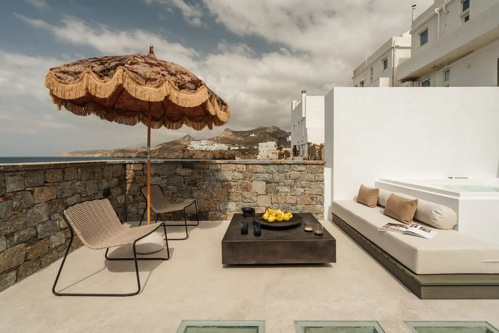 Außenbereich einer Terrasse mit Sonnenschirm, Tisch, Stühlen und Ausblick auf Naxos Stadt.